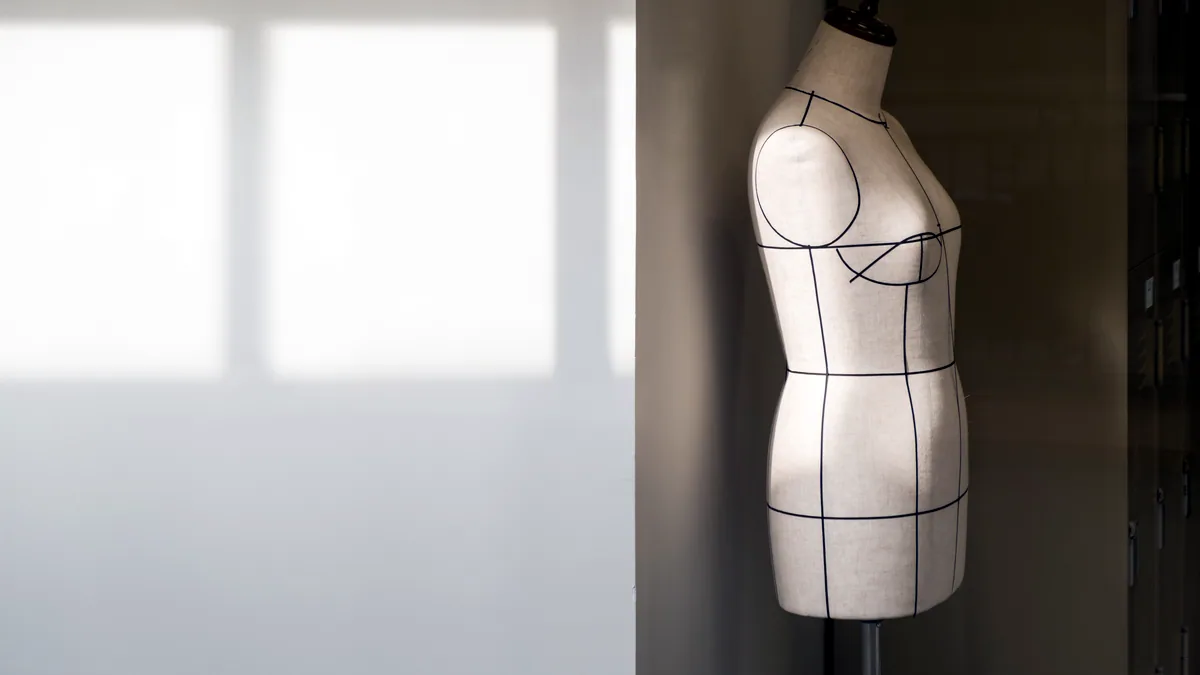 A dress form mannequin in a bright studio draped in a length of fabric.