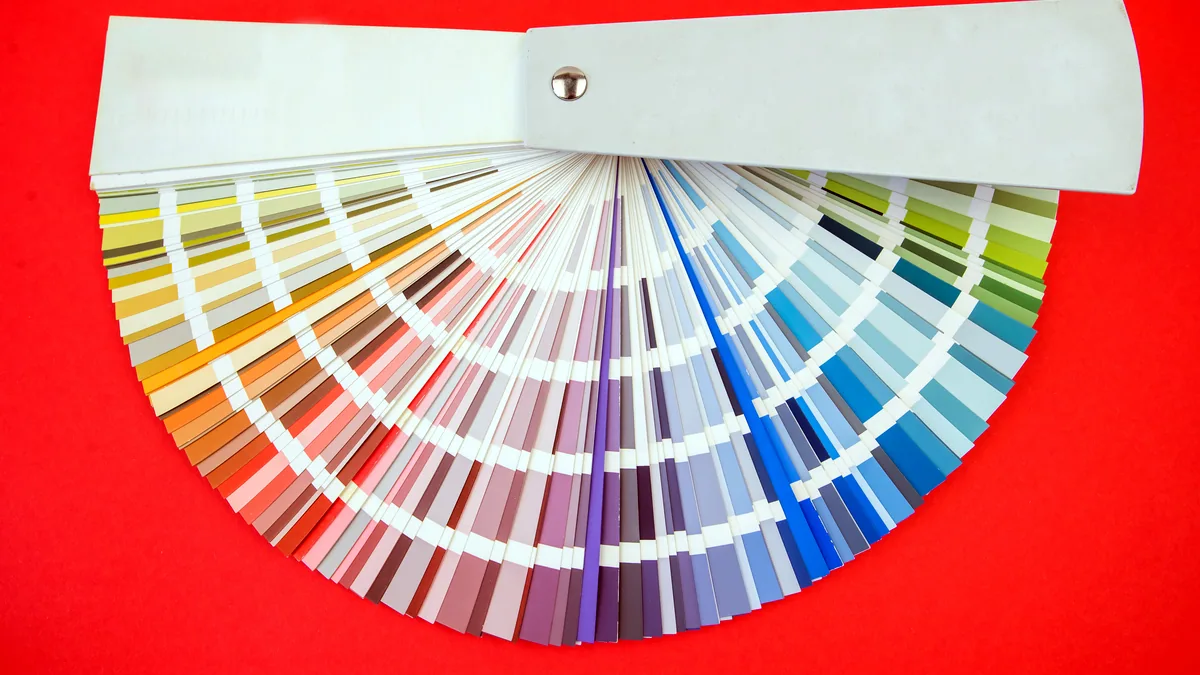 A color swatch fan open on a desk next to a fabric sample and ruler.