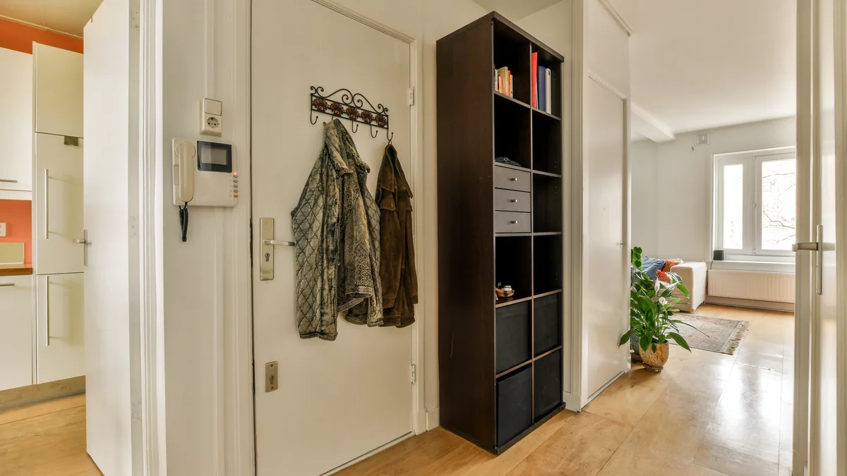 A slim compact wardrobe in a narrow hallway with a folded blanket on top.